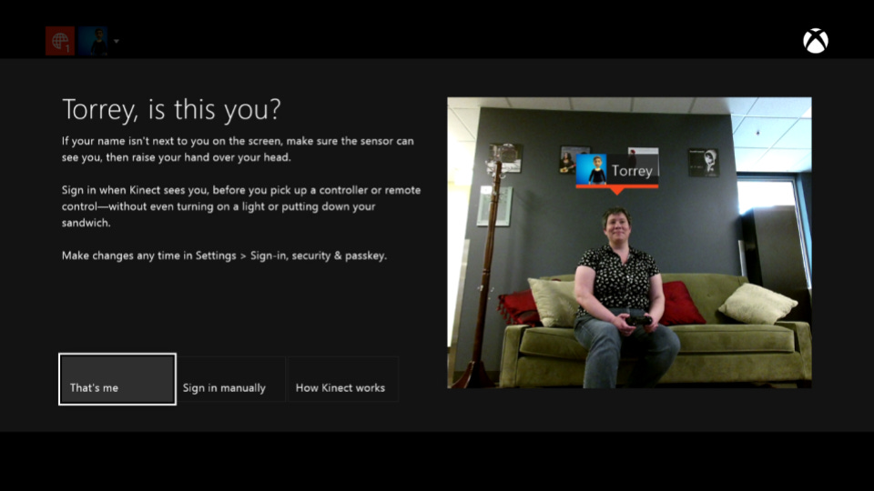 A screenshot with an image of Torrey, sitting on a green sofa and holding a controller, is shown beside Xbox text. It says: Torrey, is this you? If your name isn’t next to you on the screen, make sure the sensor can see you, then raise your hand over your head. Sign in when Kinect sees you, before you pick up a controller or remote control—without ever turning on a light or putting down your sandwich. Make changes any time in Settings > Sign-in, security & passkey. Three buttons at the bottom say: That’s me, Sign in manually, and How Kinect works. 