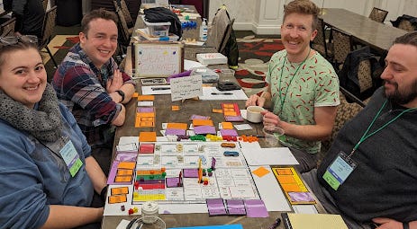 A table of players around the sprawling cutout cards of a prototype restaurant board game.
