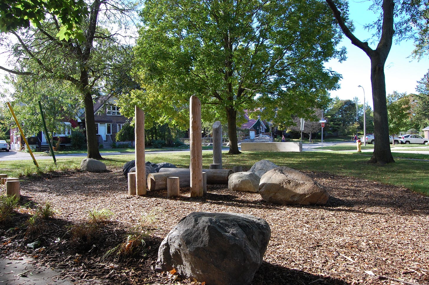 Naturalized playground including large boulders and logs and stumps for climbing.