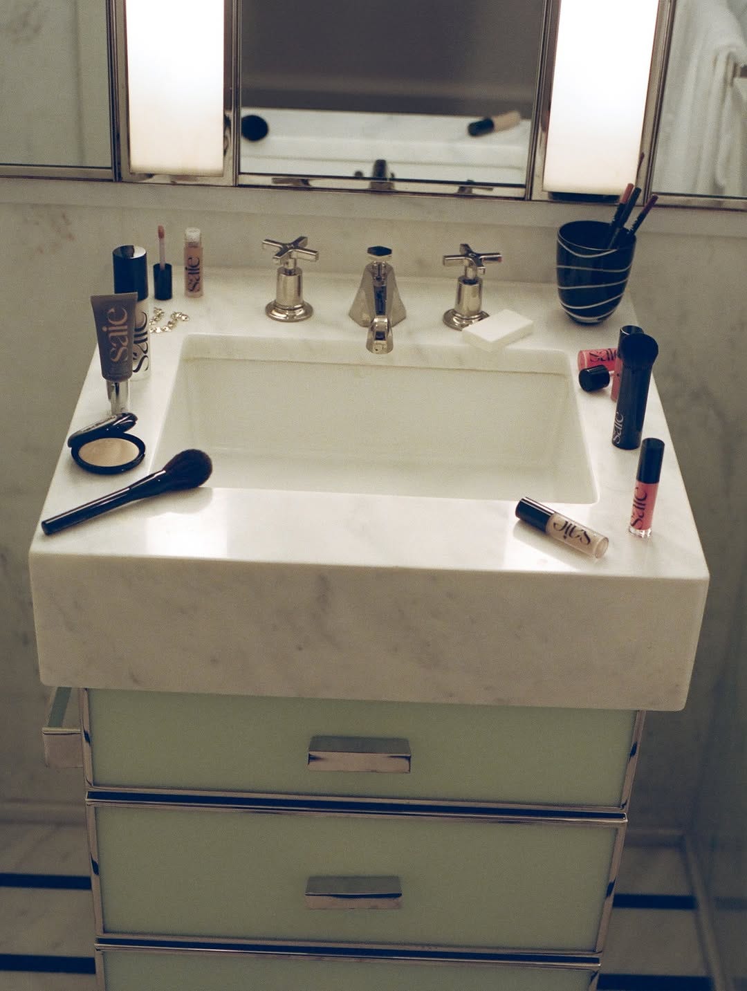A marble bathroom sink with Saie makeup scattered around the perimeter.