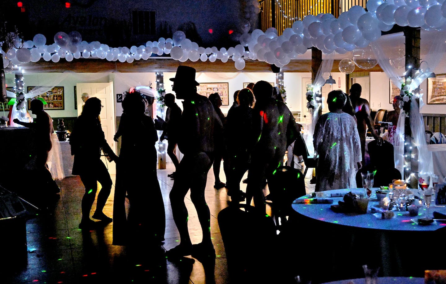 Silhouetted nude and partially dressed guests dance under string lights and white balloons during Avalon Resort’s 30th anniversary gala in Paw Paw, West Virginia. A man wearing a top hat stands at the center of the lively, dimly lit celebration. Silhouetted nude and partially dressed guests dance under string lights and white balloons during Avalon Resort’s 30th anniversary gala in Paw Paw, West Virginia. A man wearing a top hat stands at the center of the lively, dimly lit celebration.