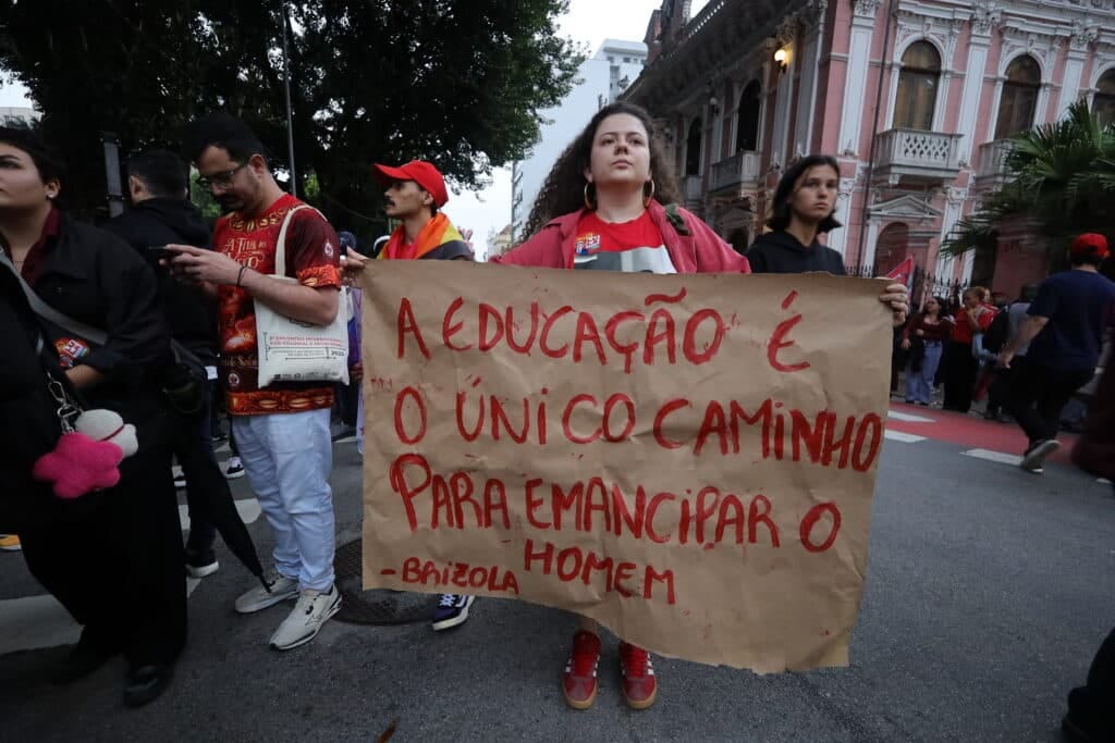 Woman at a street protest holds a sign reading "A educação é o único caminho para emancipar o homem - Brizola Woman at a street protest holds a sign reading "A educação é o único caminho para emancipar o homem - Brizola