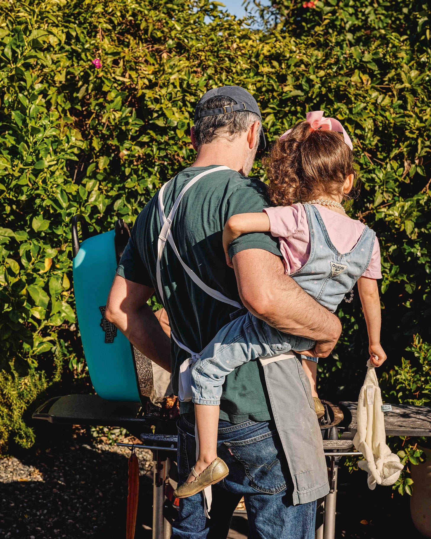 Noah holding his daughter on his hip while he grills outside.