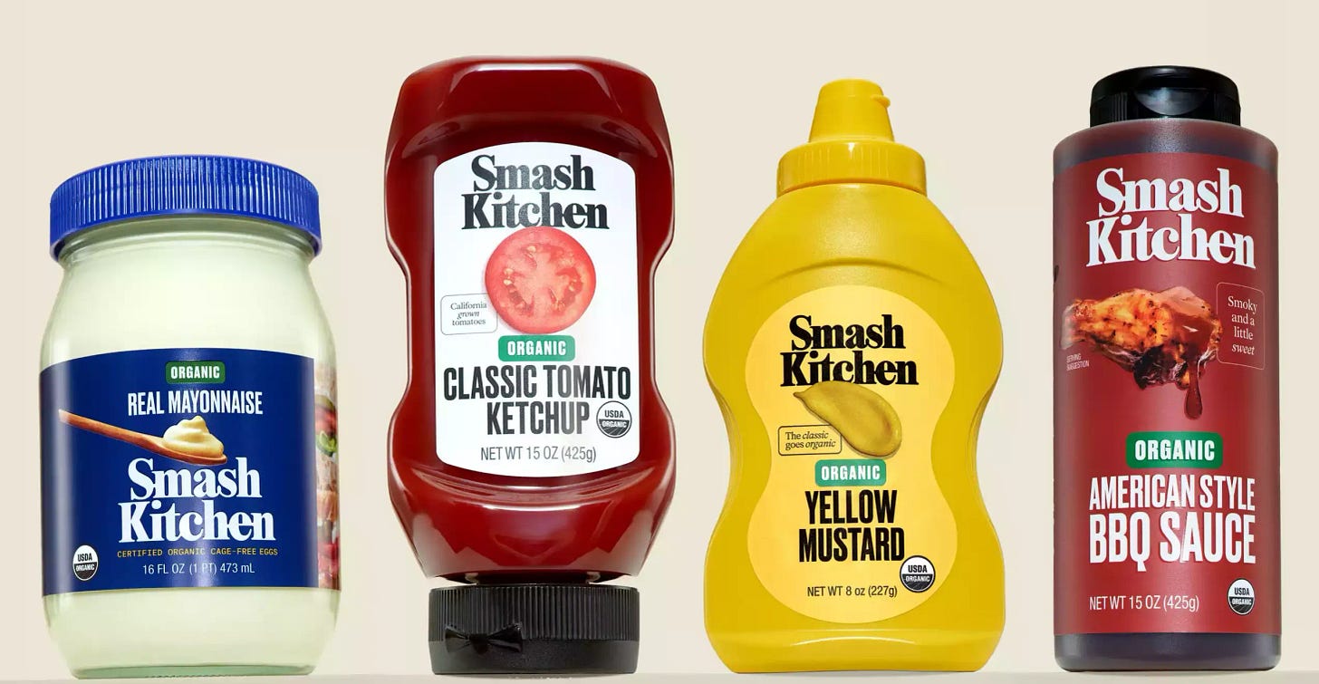Four bottles of Smash Kitchen condiments on a beige background.
