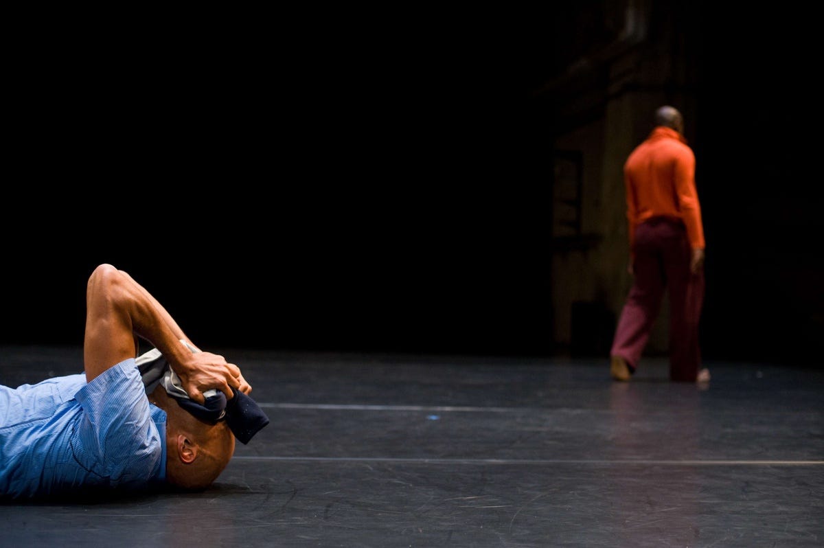 Two people on a stage, one is standing up and the other is lying down.
