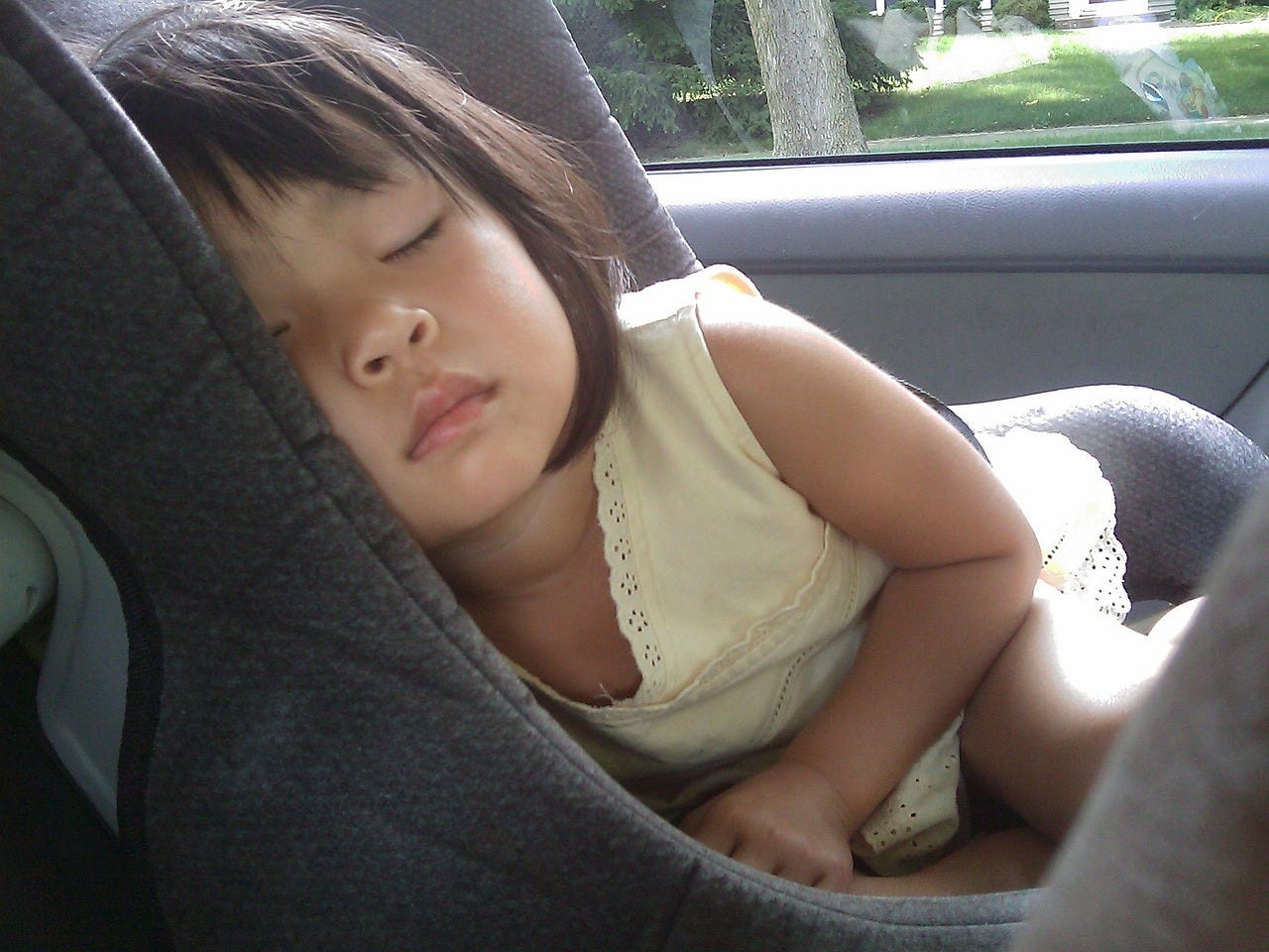Asian toddler wearing a yellow top asleep in a car seat.