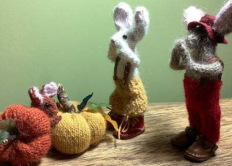 Two rabbits looking at two pumpkins, and a tiny rabbit head poking out. The bigger rabbits look shocked.