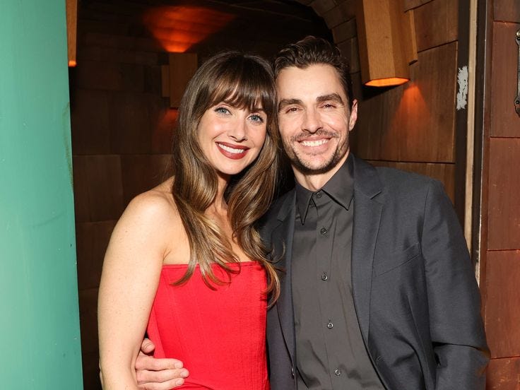 This may contain: a man and woman standing next to each other in front of a green wall at an event