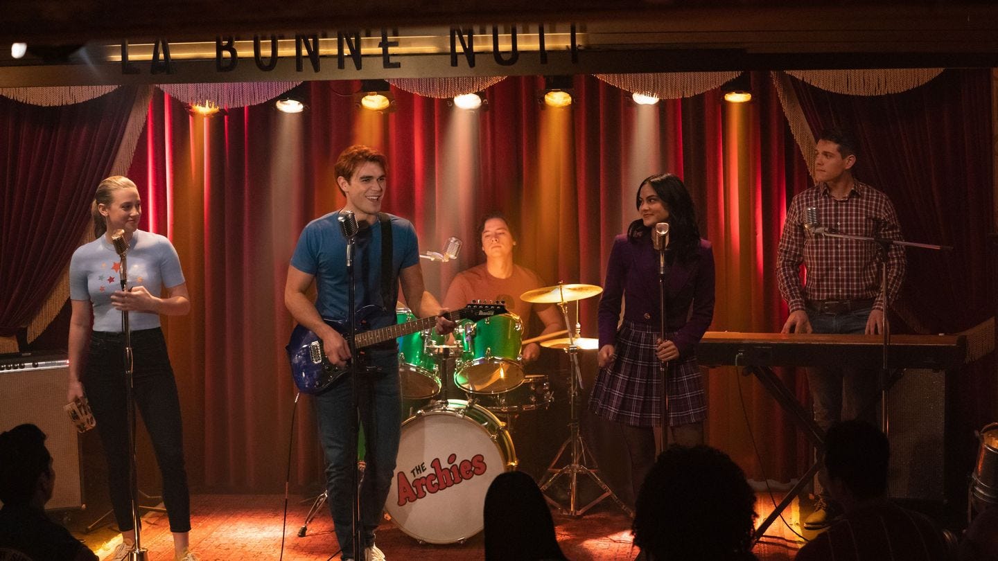 Screenshot from the TV show Riverdale. Features 5 of the shows principal characters on stage preforming as "the Archies." It looks stiff and really sort of awful, God bless them. 