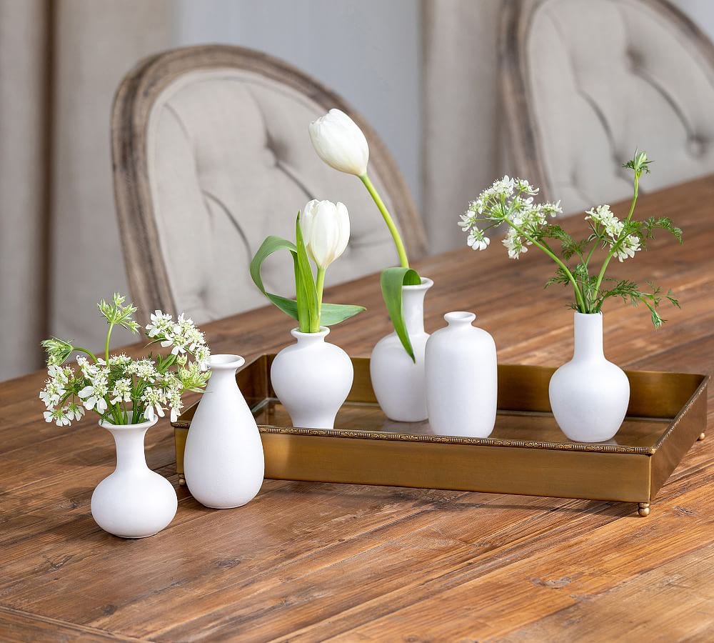A group of white vases with flowers on a wooden table

Description automatically generated