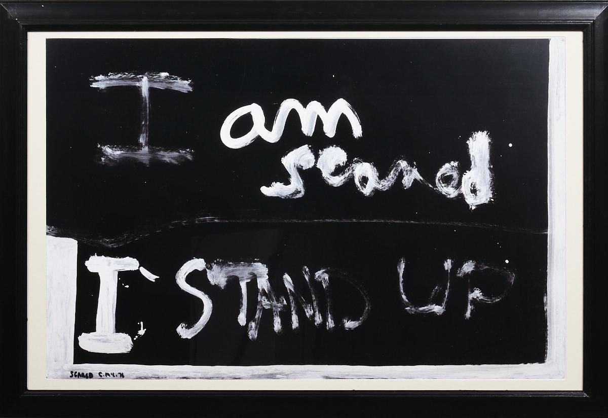 Black rectangle with the words, "I am scared" in the top of the rectangle in white, and  "I stand up" in the lower part of the rectangle also in white. The writing is in cursive hand writing in white paint.  There is a white border and black outer frame.