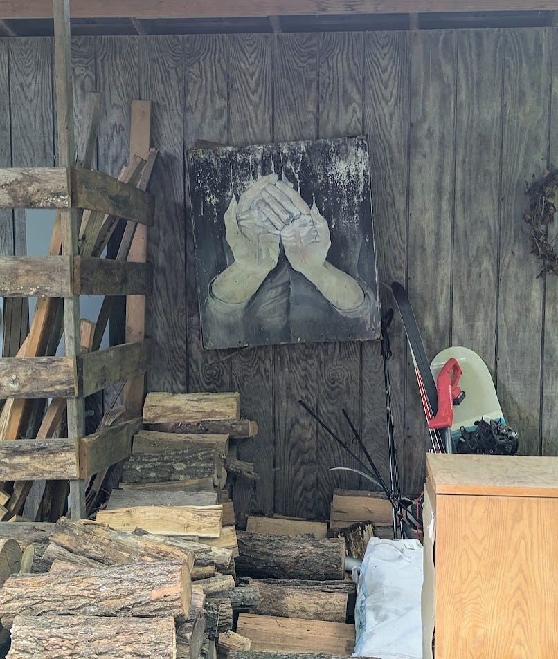 stack of firewood in woodshed with art of lifted hands next to saw