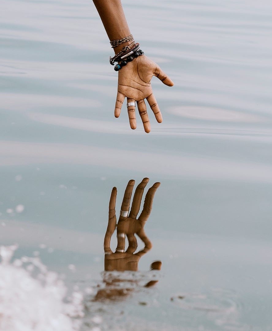 person's hand reaching on water with reflection ]