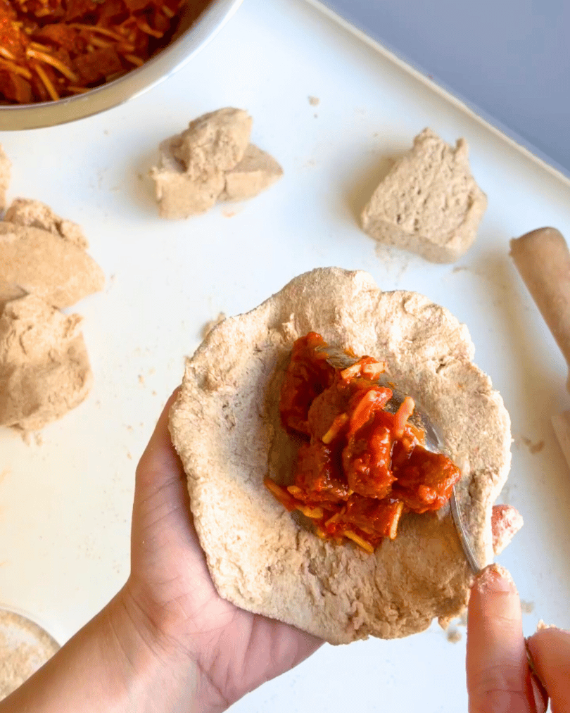 whole wheat dough being filled with tomato sauce, pepperoni, and cheese