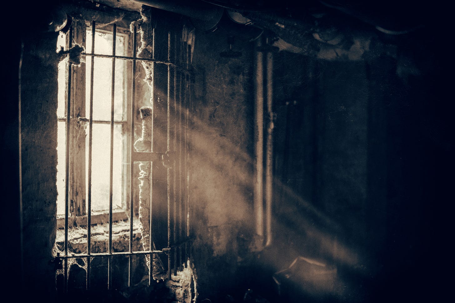 Light shines through a prison window with bars over it. The prison resembles a dungeon. Light shines through a prison window with bars over it. The prison resembles a dungeon.