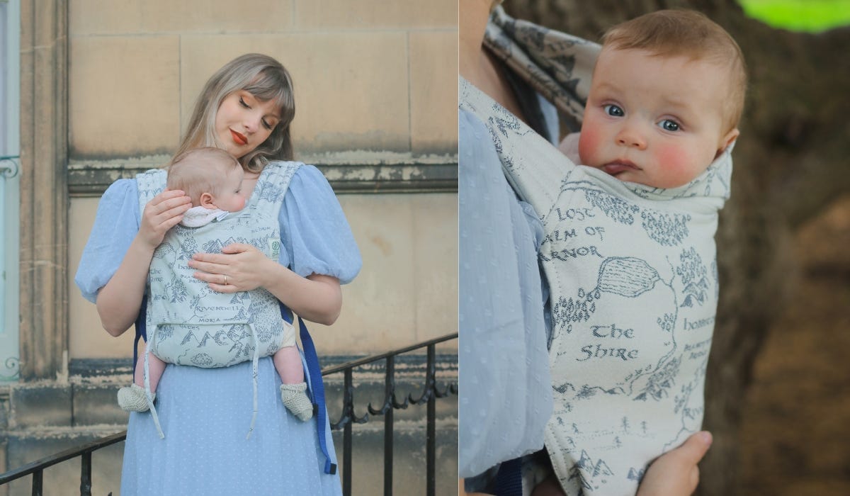 A mother carries their baby in an Oscha sling, with railings and a building in the background