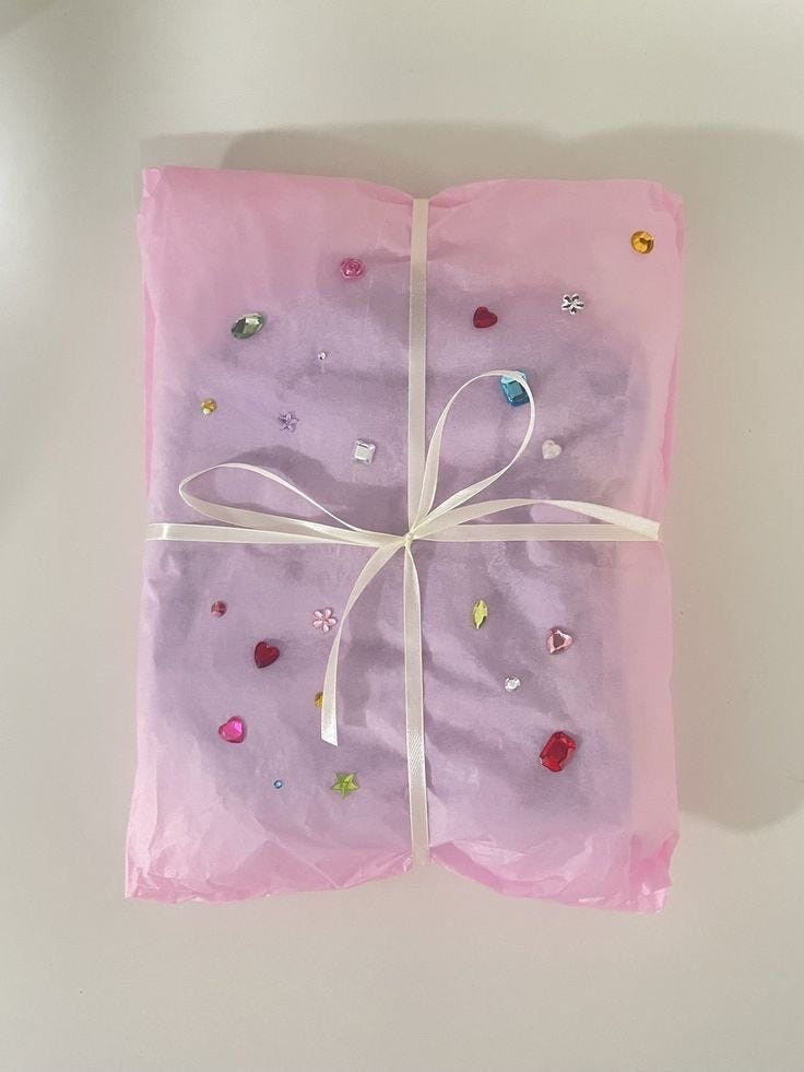 This may contain: a present wrapped in pink tissue paper with white ribbon and confetti on it