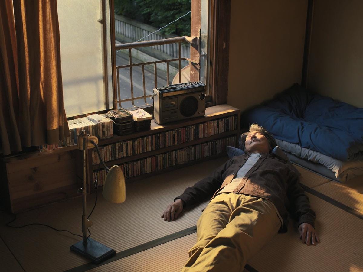 An older Japanese man, laying down on the floor of his apartment surrounded by books and vintage cassette tapes, enjoying the sunshine coming through the open window.