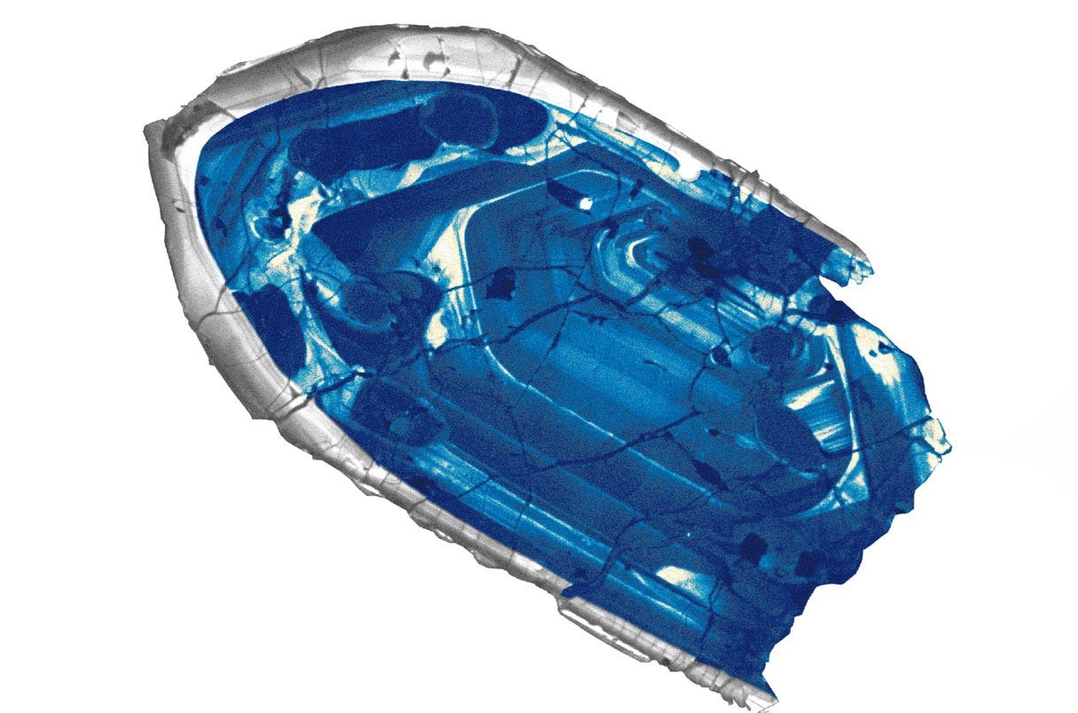 Cathodoluminescence image of a zircon grain showing concentric growth zones in shades of blue and grey against a white background. The zones record distinct episodes of crystal growth spanning billions of years, preserving geochemical information about early Earth environments that no longer exist. Cathodoluminescence image of a zircon grain showing concentric growth zones in shades of blue and grey against a white background. The zones record distinct episodes of crystal growth spanning billions of years, preserving geochemical information about early Earth environments that no longer exist.