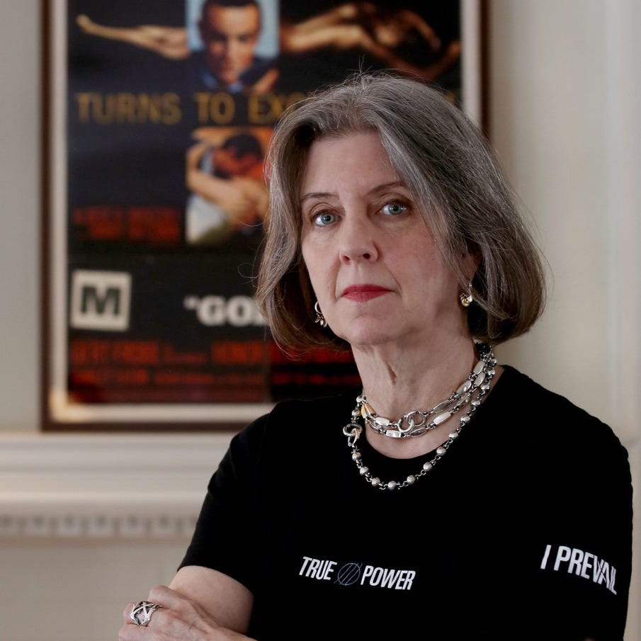 A woman stares into the camera, a movie poster on the wall behind her A woman stares into the camera, a movie poster on the wall behind her