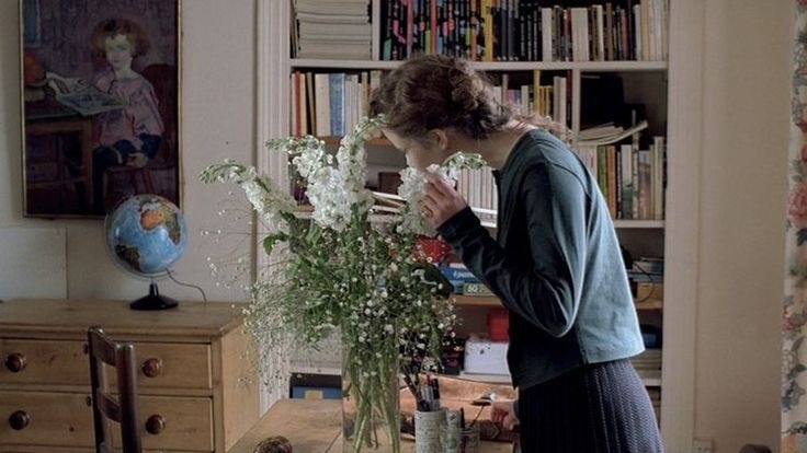 This may contain: a woman standing in front of a vase filled with flowers on top of a wooden table