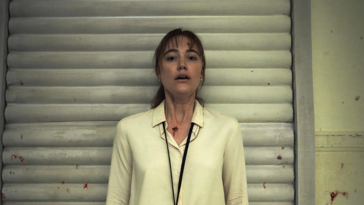 Maika Monroe looking horrified. Some sprinkles of blood on the wall behind her.