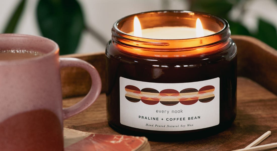 A brown double wick candle with a pink mug next to it, on top of a wooden tray A brown double wick candle with a pink mug next to it, on top of a wooden tray