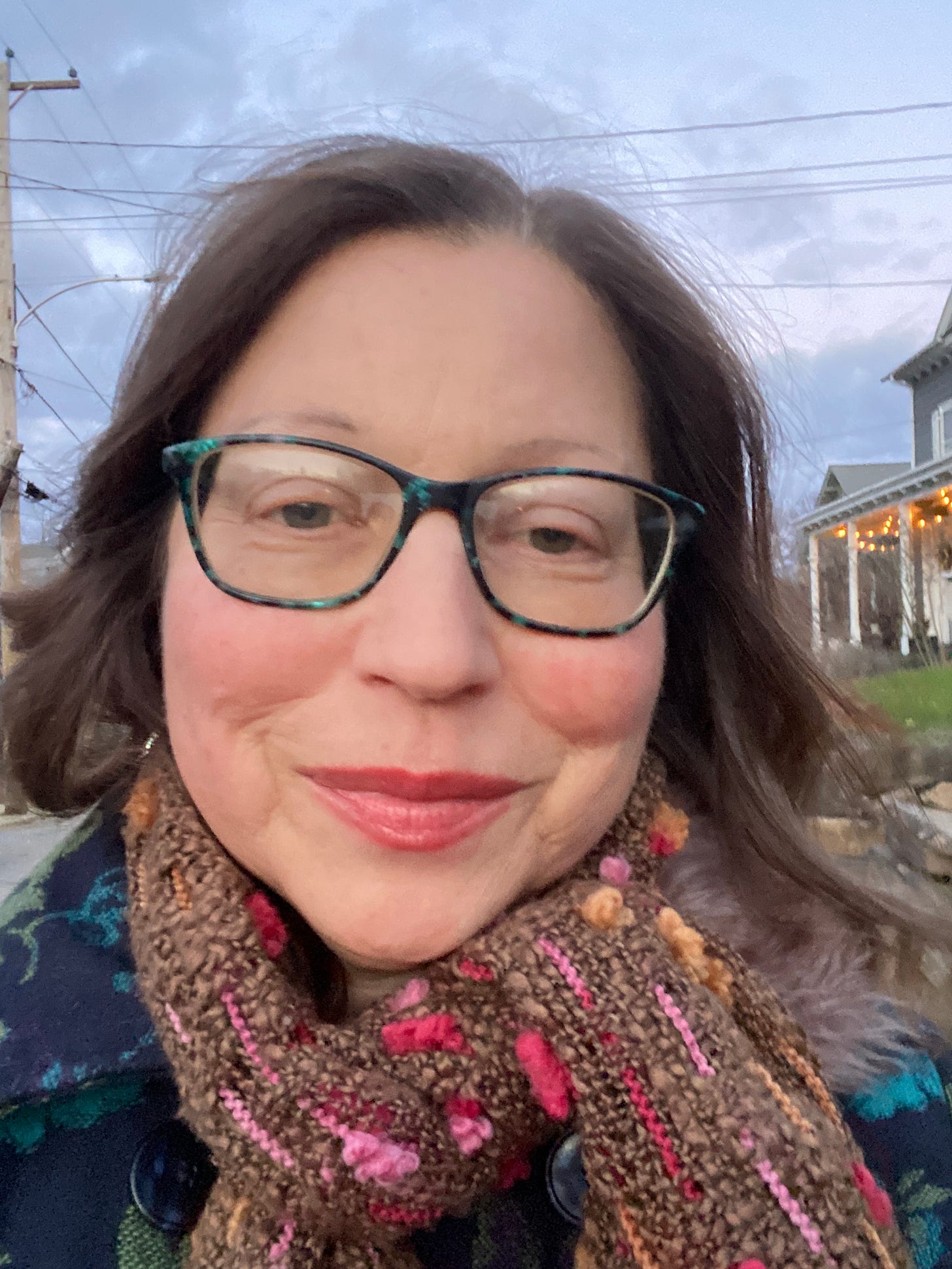 Gabrielle is a whiteskinned woman wearing glasses and smiling, a light blue sky is behind her