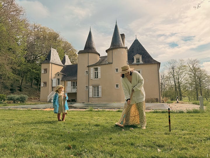 Man opening antique croquet set and woman playing croquet on a château lawn