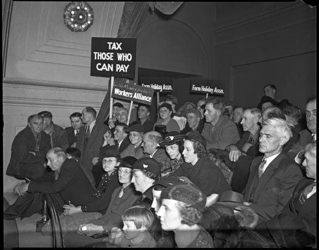 a black and white archival photo of people wearing suits and hats holding signs reading “tax those who can pay"