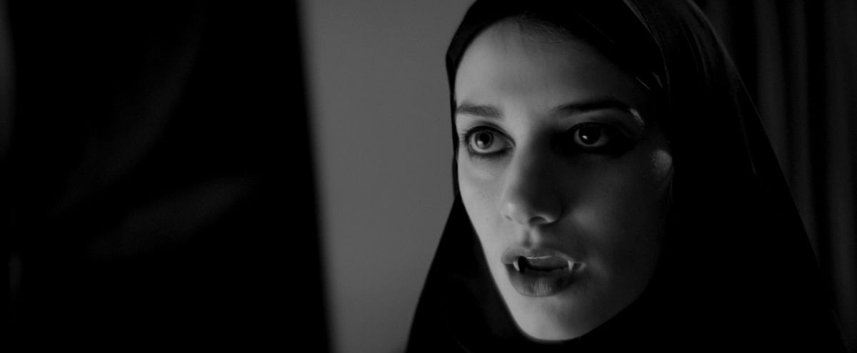 A woman in a black robe covering her head shows vampire's fangs.