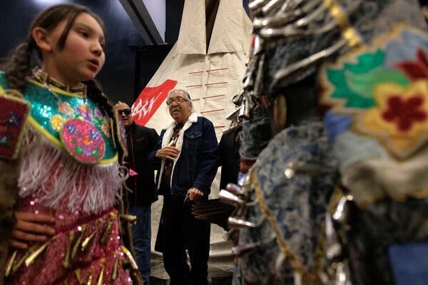 Leonard Peltier stands watching Native American dancers in colorful clothing.