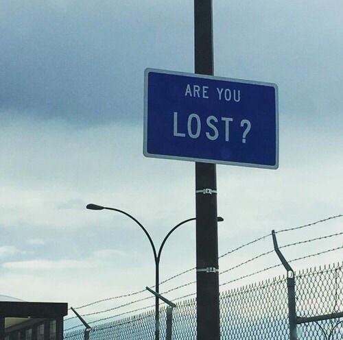 This may contain: a blue sign that says are you lost? on a pole next to a fence