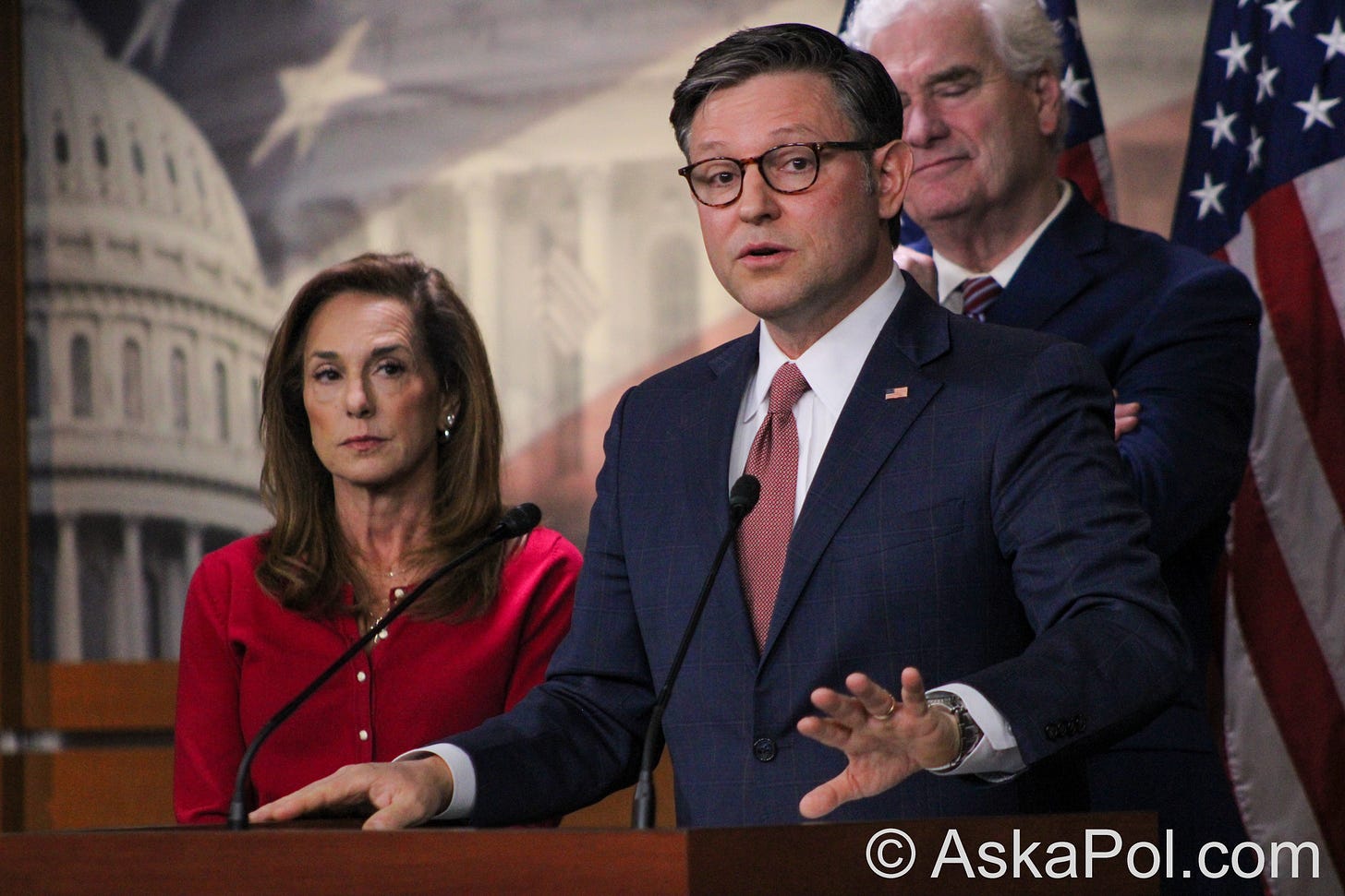 Politicians stand at a lecture addressing the media with red white and blue flag in back of them © Ask a Pol UAPs Photo by Logan Johnson