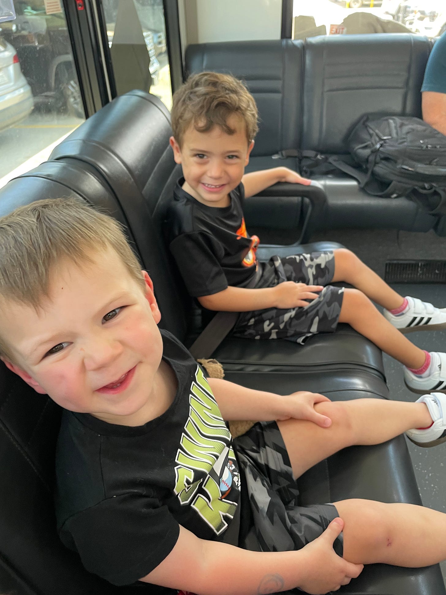 two boys riding side by side on an airport shuttle