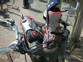 A pair of unlaced rollerblades in the metal basket of a bike.