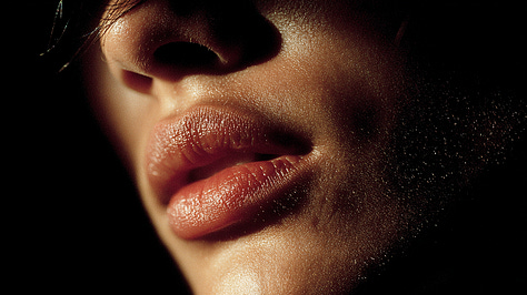 A six-image gallery showing close-up studies of Black lips in color and black-and-white, some parted as if mid-breath; silhouetted figures standing in architectural spaces divided by light and shadow; and abstract, glowing cellular forms resembling blood cells. The images move between intimacy and distance, echoing themes of voice, restraint, and survival under observation.