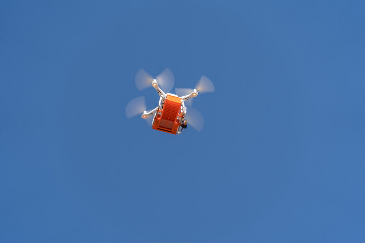 drone releasing predatory insects flies over a citrus orchard with blue skies above and green trees and farmland below. 