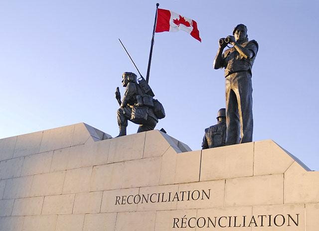 Photo of the monument which depicts three peacekeepers — two men and one woman. They stand on two edges of stone.