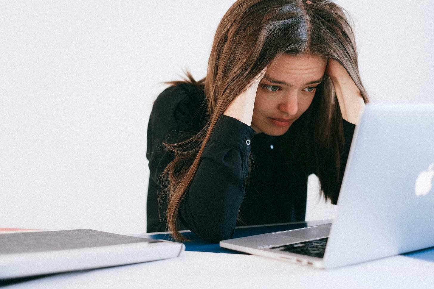 Color photograph of a woman looking stressed while looking at a laptop