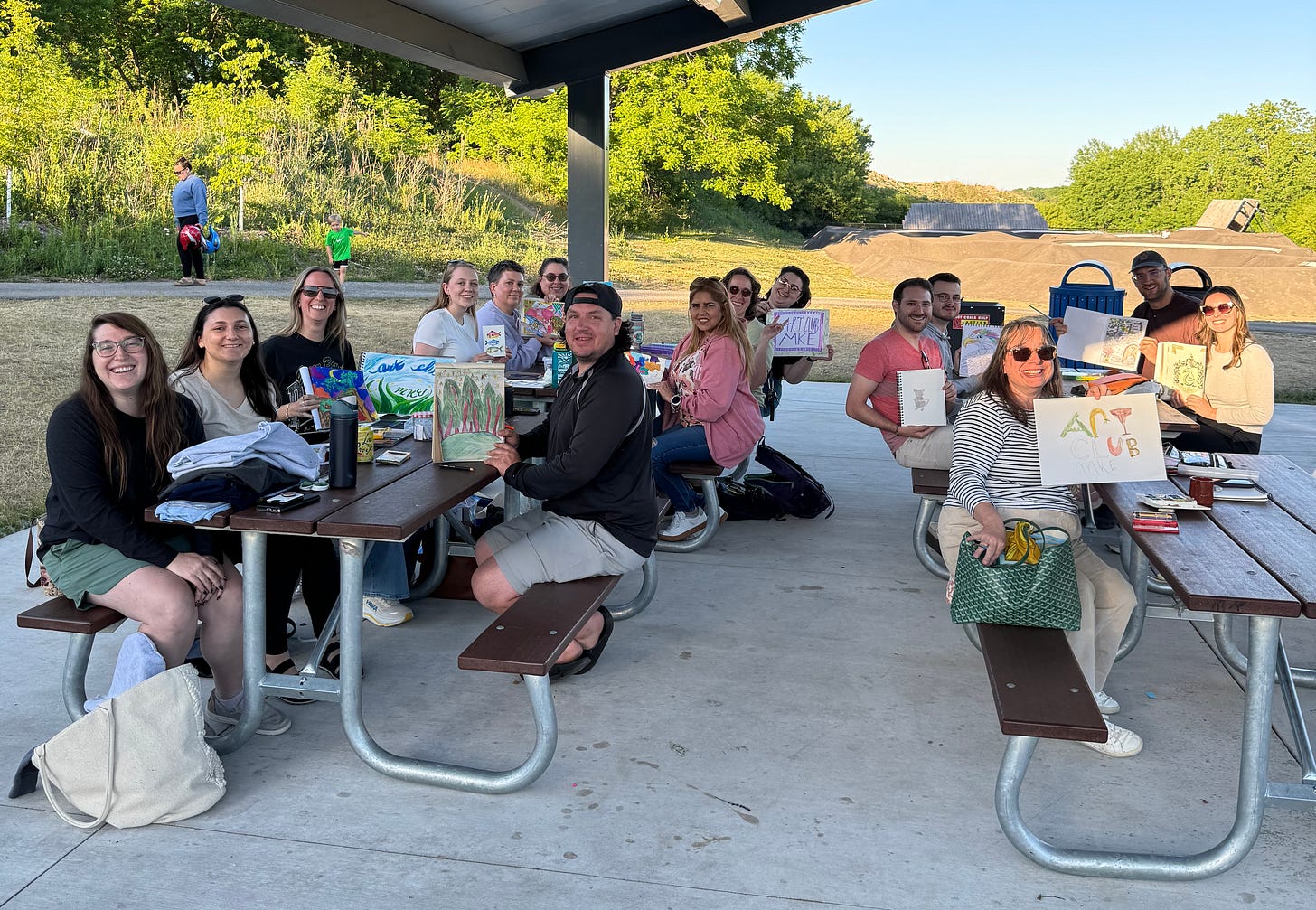 A bunch of happy adults showing their art in an outdoor shelter at a park
