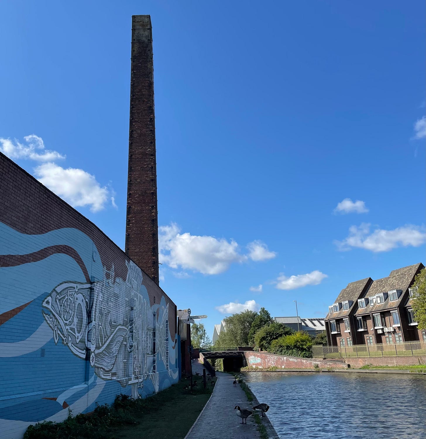 The canal at Walsall in the sunshine, with an old industrial chimney in the background and a mural in the foreground