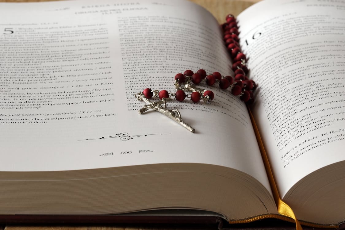Free Open Bible with red rosary beads draped on pages, symbolizing faith and devotion. Stock Photo