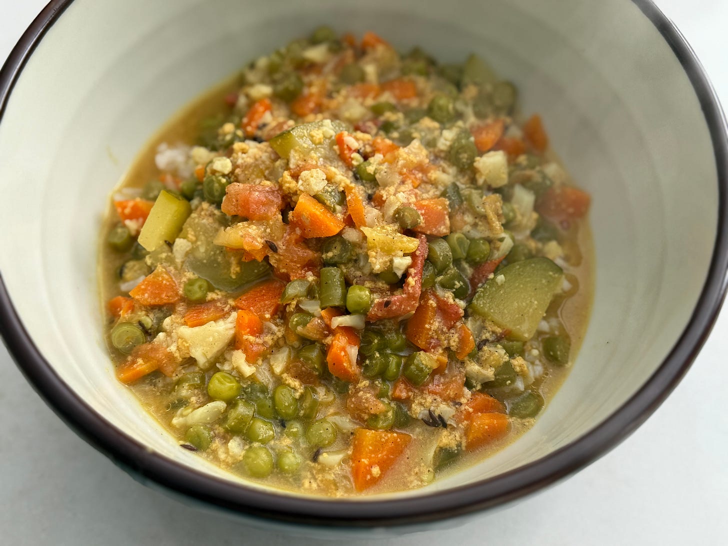Steaming bowl of mixed vegetable curry—peas, carrots, cauliflower, and zucchini—in a creamy spiced sauce over rice.