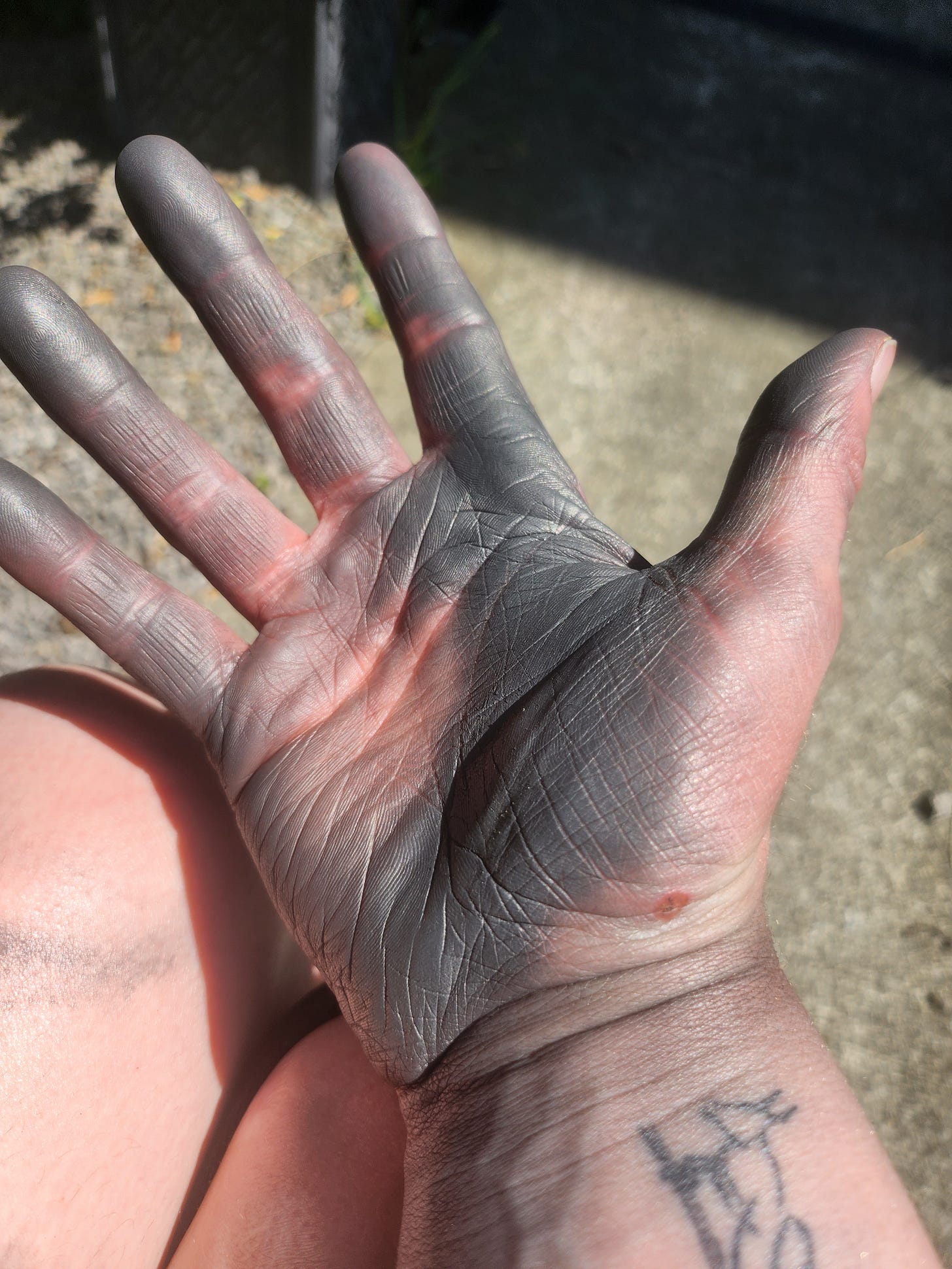 A photo of my hand outstretched. My palm is covered in a metallic layer of dust, which is embedded into my skin. 