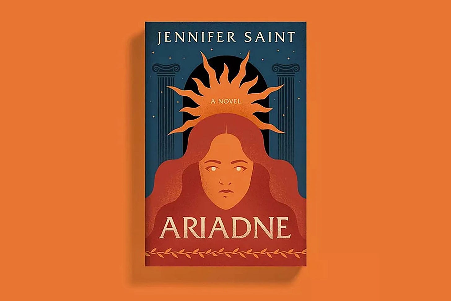 Fundo laranja, capa do livro acima do fundo laranja. Ariadne, uma novela de Jennifer Saint. A Capa tem fundo azul escuro, pilastras gregas e uma representação de Ariadne, na cor laranja, à frente. A coroa de Ariadne se junta ao fundo para criar um coroa de estrelas.