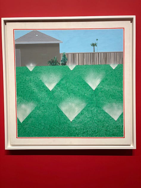 Multiple bright-colored paintings including a self-portrait of Hockney in a yellow plaid suit and big yellow glasses, the crowd viewing paintings, a mother and child in front of a bright painting of a massive tree, an annunciation painting redone in neon colors, a green lawn with sprinkler spray, a photograph of hockney working at his drawing table with his little terrier dog under the table and two paintings with raindrops hitting puddles among trees