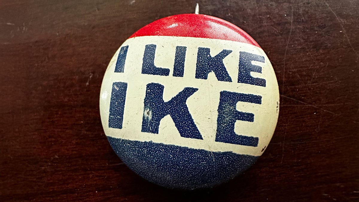 A vintage red, white, and blue 'I Like Ike' campaign button resting on a dark wood surface.