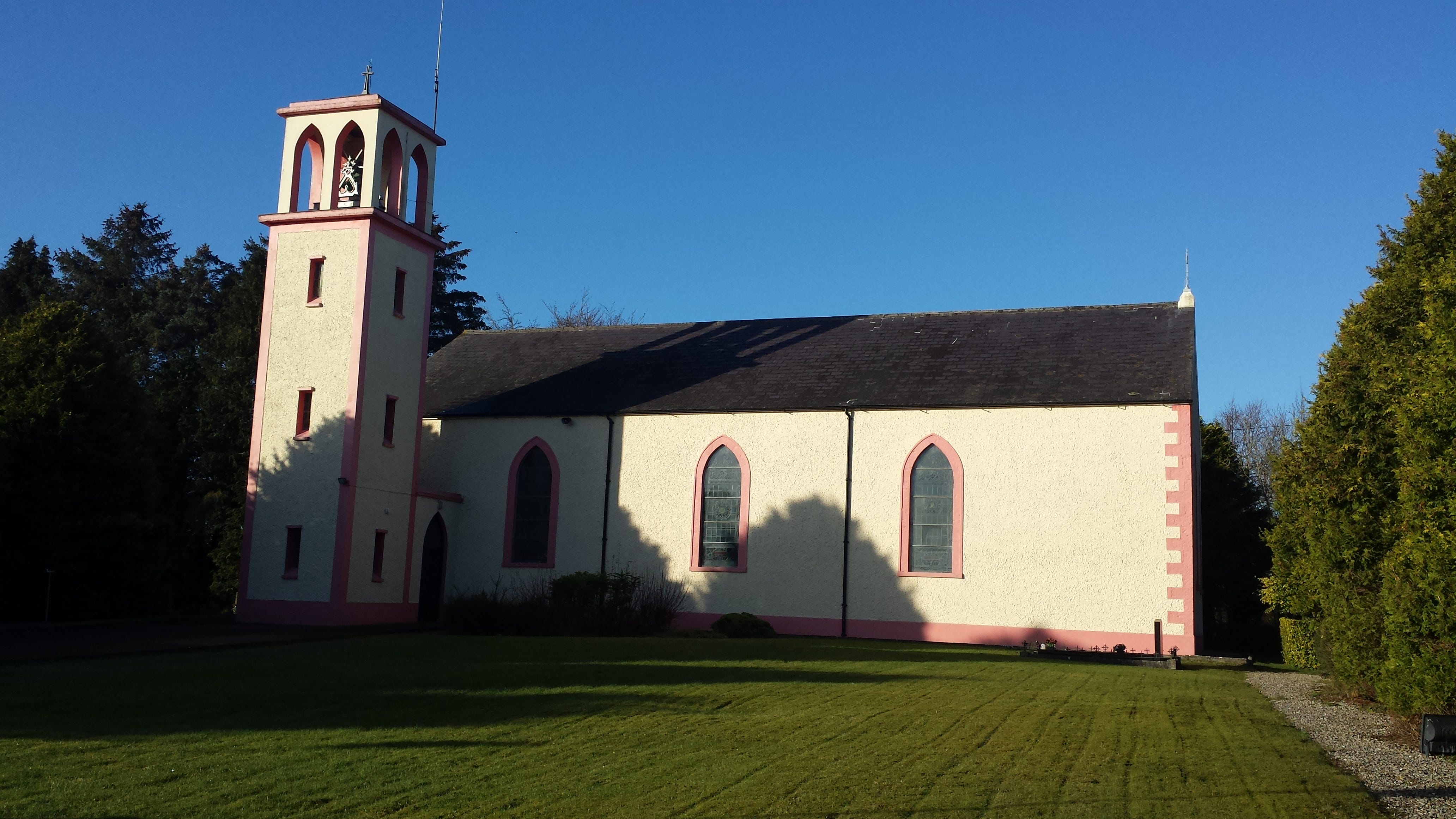 Plain, yellow-painted church with three arched windows and small bell tower atached to left of building.