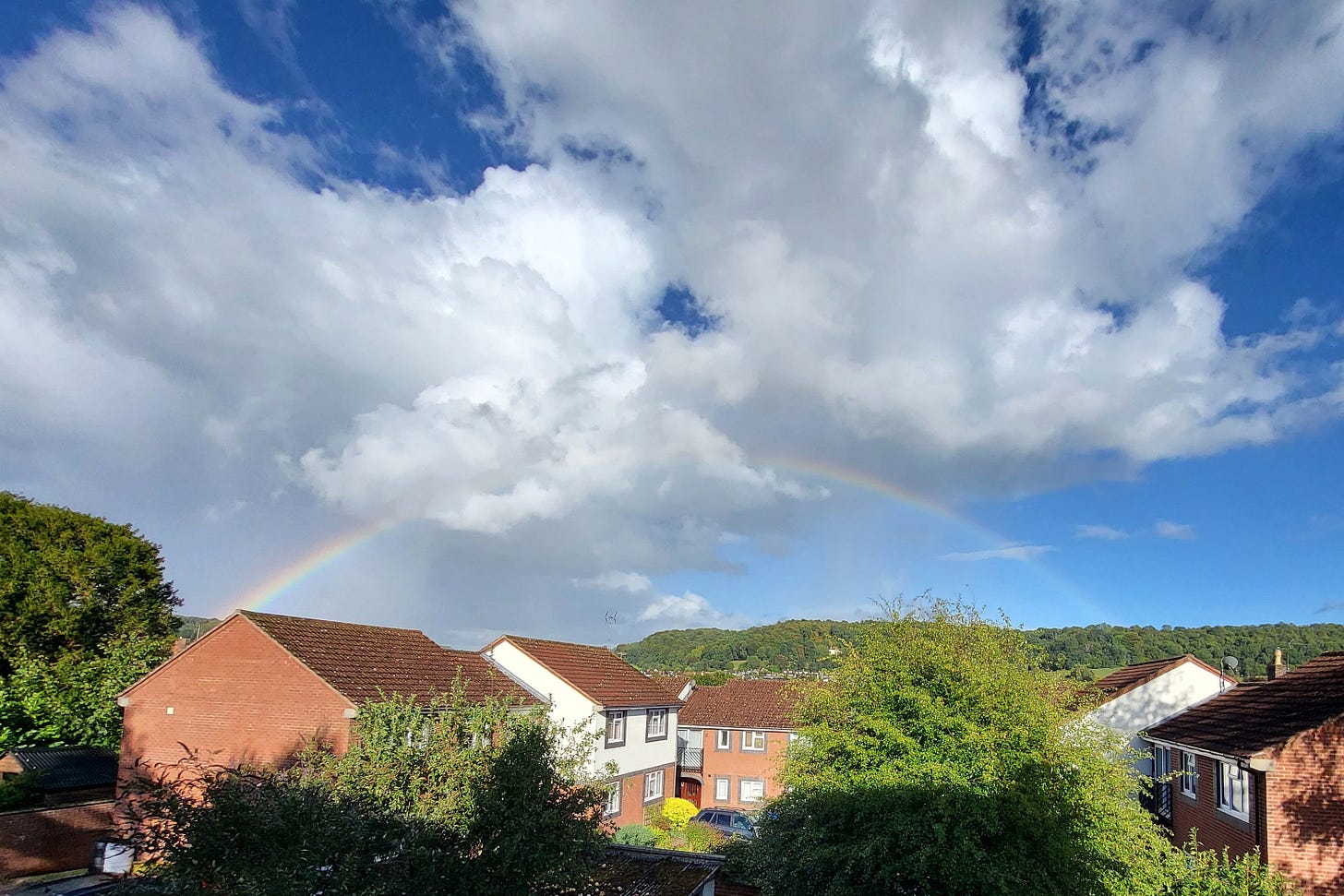 A rainbow above a hill, slightly covered by large cumulus clouds